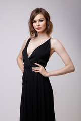 High fashion photo of a beautiful elegant young woman in a pretty black evening party dress with a deep neckline posing on white background. Slim figure, hairstyle, studio shot. 