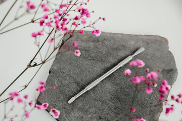A nail care tool, a pusher lies on a gray stone surrounded by pink flowers. Background
