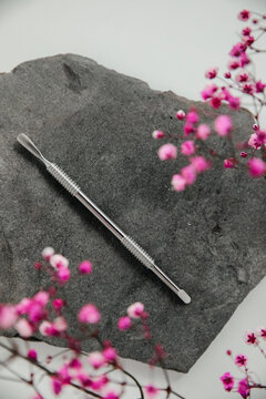 A nail care tool, a pusher lies on a gray stone surrounded by pink flowers. Background