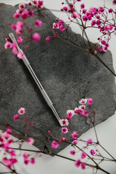 A nail care tool, a pusher lies on a gray stone surrounded by pink flowers. Background