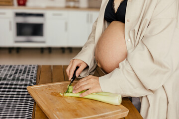A pregnant girl in home clothes prepares healthy food.