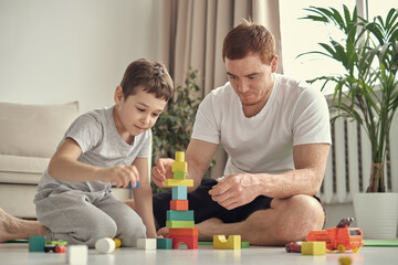 Obraz premium smiling father and little son playing with colorful blocks together at home. Playtime. diverse family