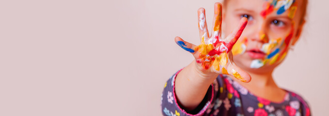 Hands and face of cute young girl painted in colorful paints. Children's makeup. Copy space.