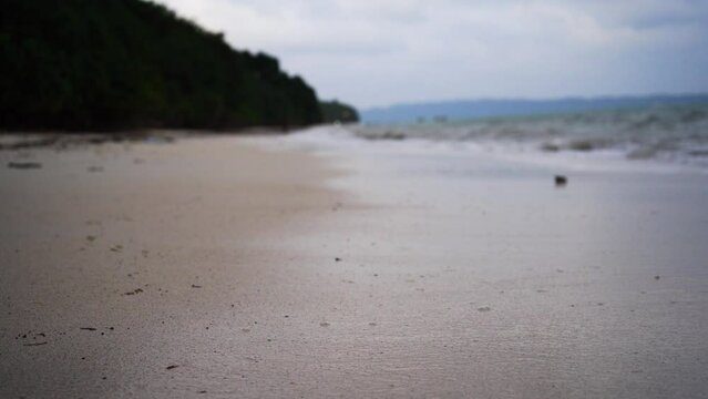low ground macro shot showing the waves coming into white sand beach with tree covered hill in distance on empty beach in havelock andaman nicobar island India