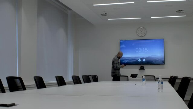 An Asian office employee pacing around an empty boardroom while texting on his mobile phone, the man focused on his screen and oblivious to his surroundings