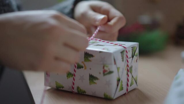 Hands tie ribbon around a wrapped christmas gift, close up
