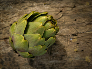 Fototapeta premium Fresh cut organic green yellow artichoke on a unfocused rough wooden board. Healthy food on rustic background