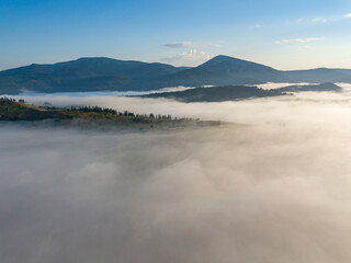 Obraz na płótnie Canvas Flight over fog in Ukrainian Carpathians in summer. Mountains on the horizon. A thick layer of fog covers the mountains with a continuous carpet. Aerial drone view.