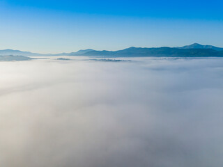 Flight over fog in Ukrainian Carpathians in summer. Mountains on the horizon. A thick layer of fog covers the mountains with a continuous carpet. Aerial drone view.
