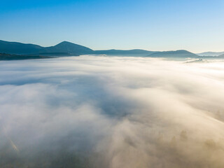 Flight over fog in Ukrainian Carpathians in summer. Mountains on the horizon. A thick layer of fog covers the mountains with a continuous carpet. Aerial drone view.
