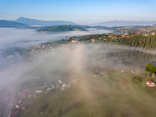 Mountain settlement in the Ukrainian Carpathians in the morning mist. Aerial drone view.