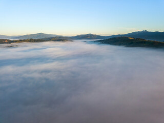 Flight over fog in Ukrainian Carpathians in summer. Mountains on the horizon. A thick layer of fog covers the mountains with a continuous carpet. Aerial drone view.