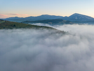 Obraz premium Flight over fog in Ukrainian Carpathians in summer. Mountains on the horizon. A thick layer of fog covers the mountains with a continuous carpet. Aerial drone view.