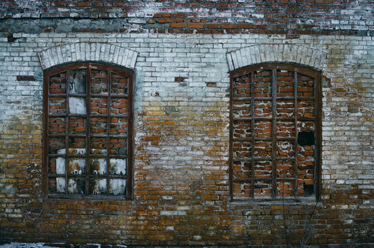 The Wall Of An Old Abandoned Factory, The Arched Windows Are Bricked Up, But The Wooden Frames Remain, The Brickwork Was Once Painted, The Paint Has Long Since Peeled Off In Places