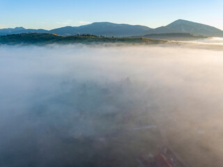 Sunny morning in the foggy Carpathians. A thick layer of fog covers the mountains. Aerial drone view.