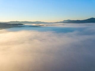 Flight over fog in Ukrainian Carpathians in summer. Mountains on the horizon. A thick layer of fog covers the mountains with a continuous carpet. Aerial drone view.