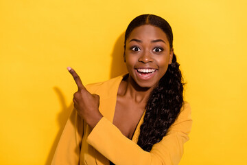 Portrait of beautiful trendy cheerful wavy-haired girl showing copy blank space isolated on bright yellow color background