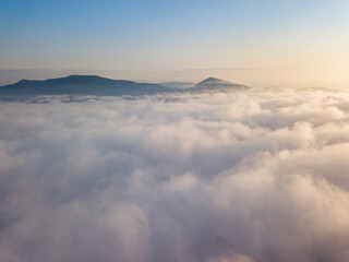 Flight over fog in Ukrainian Carpathians in summer. Mountains on the horizon. Aerial drone view.