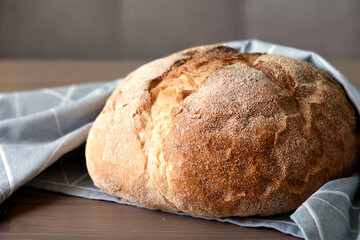 Loaf of freshly baked homemade artisan bread in linen towel on a wooden surface. Selective focus.