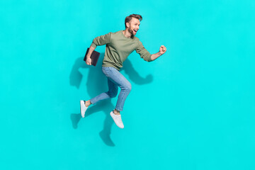 Full body photo of young blond guy jump with laptop wear sweater jeans sneakers isolated on turquoise background