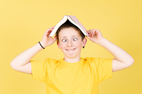 Boy holding a book on head and making funny face isolated on yellow background