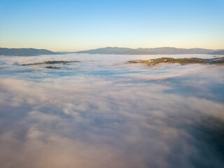 Flight over fog in Ukrainian Carpathians in summer. Mountains on the horizon. A thick layer of fog covers the mountains with a continuous carpet. Aerial drone view.