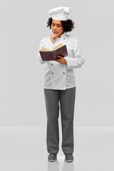 cooking, culinary and people concept - thinking female chef in white toque and jacket reading cook book over grey background