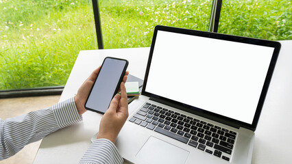 woman holding a blank white screen mobile phone at a desk with laptop with a white screen blank copying with internet technology concept