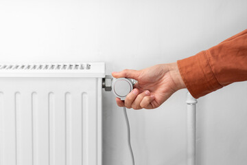 heating, energy crisis and consumption concept - close up of hand turning radiator toggle switch at...