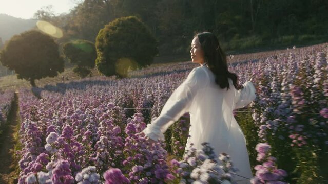 Young asian woman runs in flower field on sunset