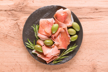 Charcuterie board with proscuitto served with olives on wooden table. Black plate with traditional italian antipasti. Selective focus