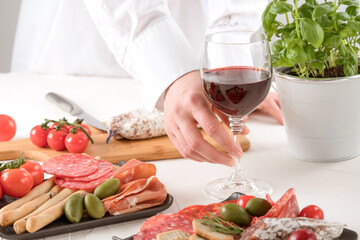 Woman serving traditional Italian antipasti at home or restaurant kitchen. Charcuterie plate with different types of sausages - salami, bresaola, proscuitto served with olives, tomatoes and grissini