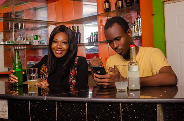 lady smiling having a drink while her friend is excited about what he saw on his cellphone