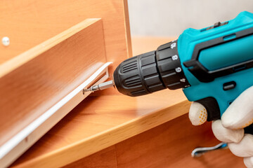 The master uses a cordless screwdriver to repair the drawer from the desk