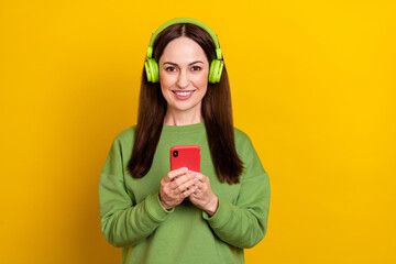 Portrait of attractive trendy cheerful woman listening single using device post isolated over bright yellow color background
