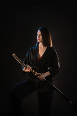 Young beautiful woman in black kimono with katana on black background