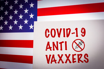 Conceptual keyword COVID-19 ANTI VAXXERS on card on an US flag background. Anti coronavirus vaccination concept.