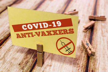 Conceptual message card showing COVID-19 ANTI VAXXERS on shabby wooden table. Nice wooden clothespin or natural wooden pinch holding yellow paper note.