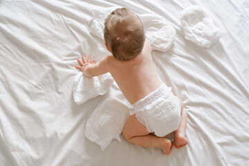 Cute baby in dry soft diaper on white bed at home, top view