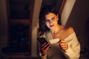 Woman using a smartphone and a credit while relaxing at home in the night