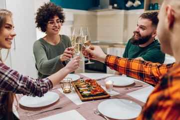 Friends sitting at a kitchen table and toasting during a dinner part