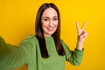 Self-portrait of attractive cheerful woman good mood showing v-sign isolated over bright yellow color background