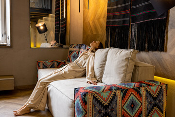 Young woman sitting relaxed on couch at modern living room in warm colors. Concept of home comfort...