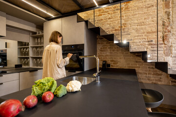 Woman preparing some food from fresh ingredients, opening oven at kitchen. Concept of healthy...