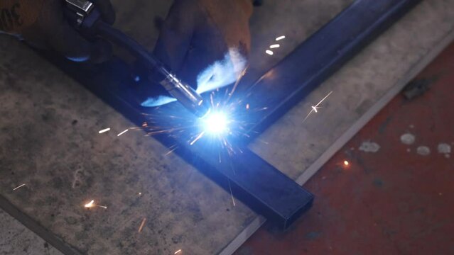 Workers splicing steel with welding ignition in a dim factory workshop