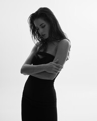 Fototapeta premium Portrait of young attractive woman model with brown long curly hair, black dress, long legs with tan skin, slim body. The concept of a beautiful elegant figure, body positive, healthy lifestyle.