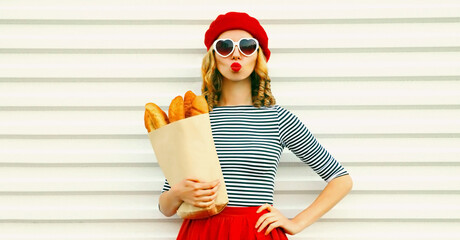 Portrait of beautiful woman blowing her red lips sending sweet air kiss holding grocery shopping...