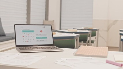 No people slowmo of test papers and laptop with monthly calendar and schedule on desktop on teachers desk in empty classroom
