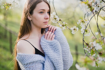 Young pretty emotional caucasian woman with long hair wearing natural makeup in romantic casual clothes walking among spring mountains near the beautiful fresh blooming tree in the countryside.