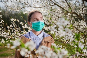 Woman allergic suffering from seasonal allergy at spring, posing in blossoming garden at...